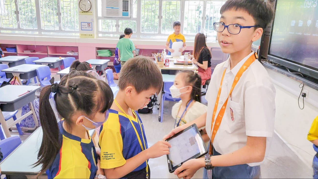 高年級同學指導低年級同學用平板電腦玩語文遊